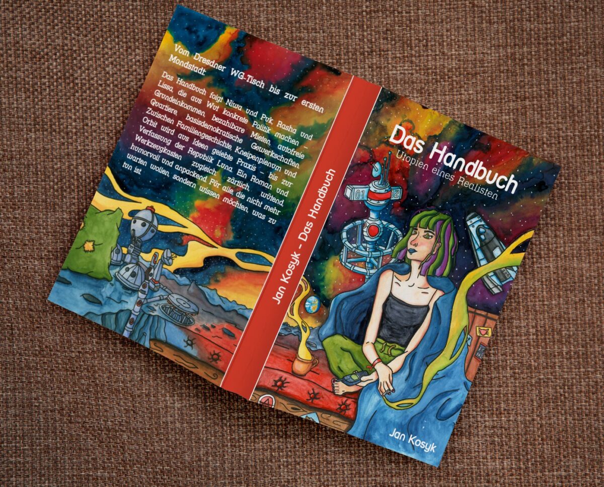 Buch "Das Handbuch – Utopien eines Realisten", aufgeschlagen liegend mit dem Cover nach oben.